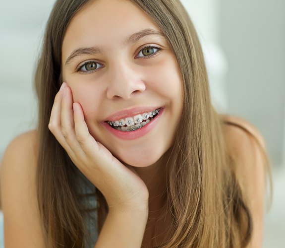 Young girl lying down and smiling with traditional metal braces in Lake Zurich, IL