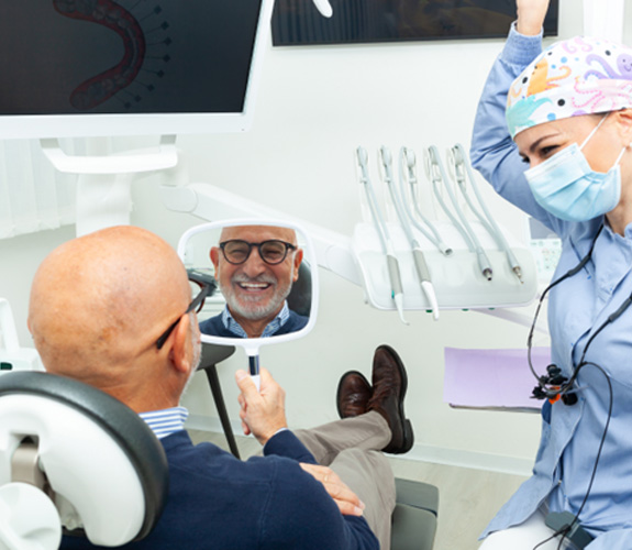Man admiring smile in mirror at dentist’s office 