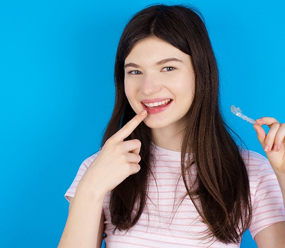 Teenage girl smiling and holding a clear aligner