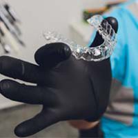 Black gloved hand holding a clear aligner