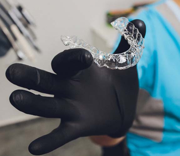 Gloved hand holding aligner for Invisalign Teen in Lake Zurich, IL