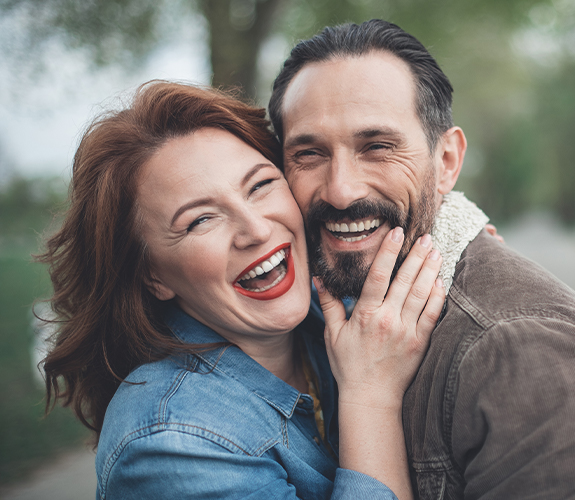 Man and woman with flawless smiles after dental implant tooth replacement