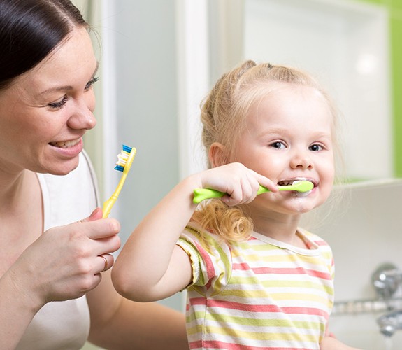 Mother helping blonde little girl brush her teeth