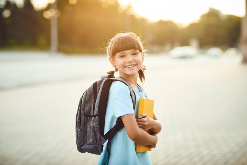Little girl with a backpack carrying a book for school