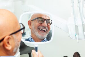 older man wearing glasses and smiling at the dentist
